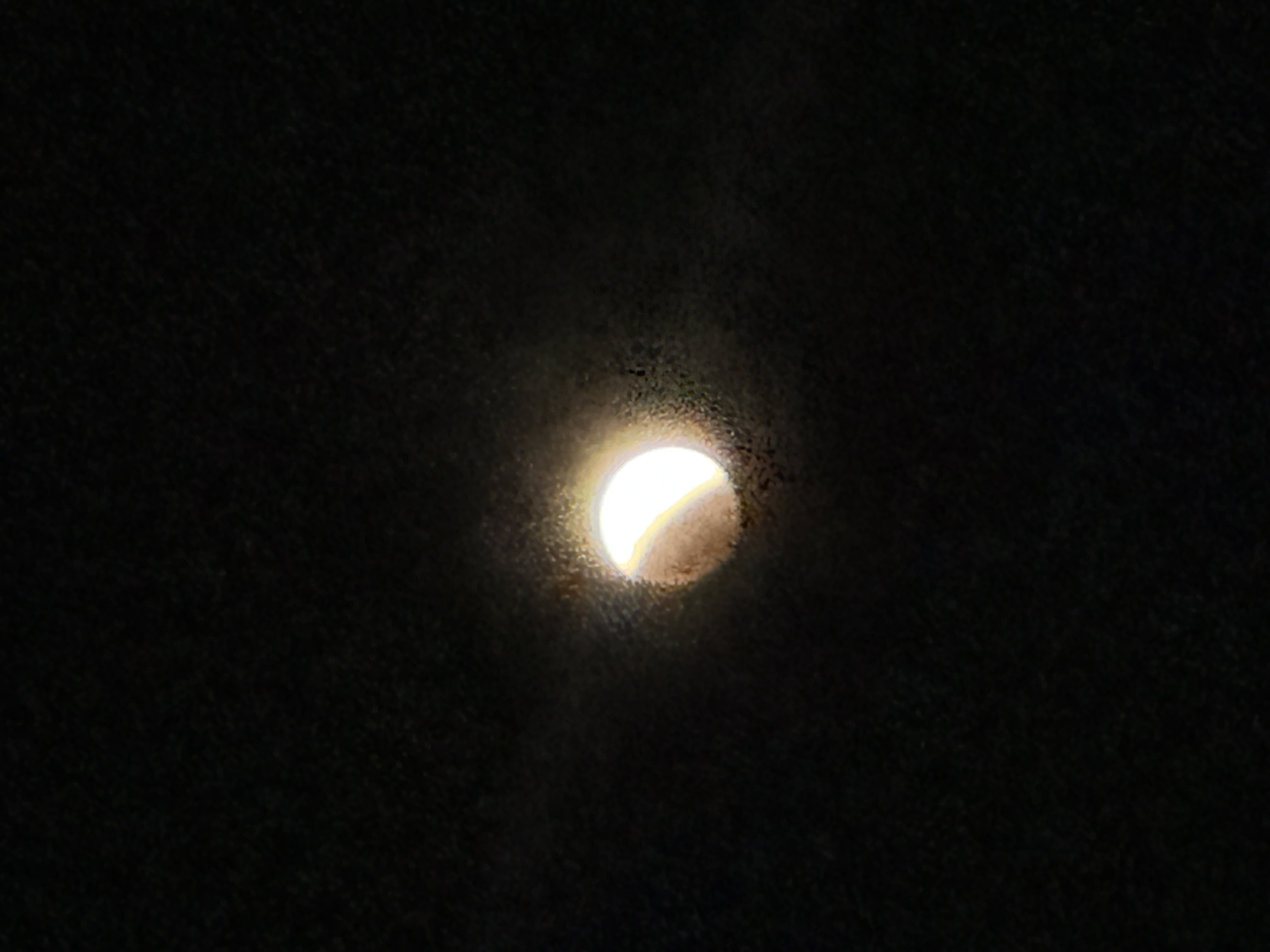 A bright light seen through a small fogged opening in a dark surface